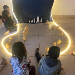 niños sentados mirando unos conos de papel y luces