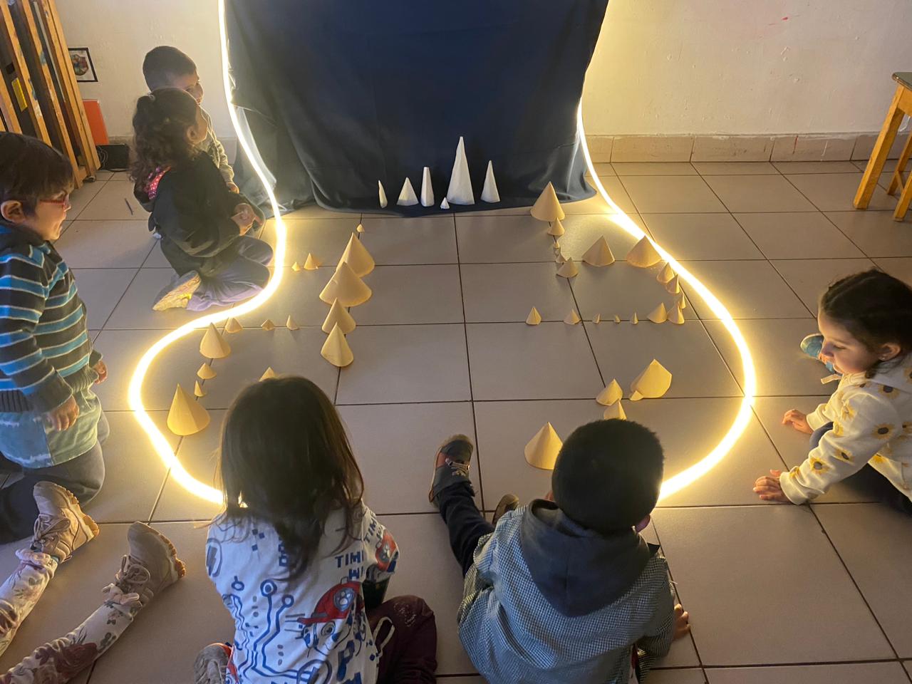 niños sentados mirando unos conos de papel y luces