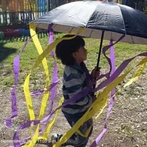 Niños jugando en jardín con paragua con tiras morada y amarilla