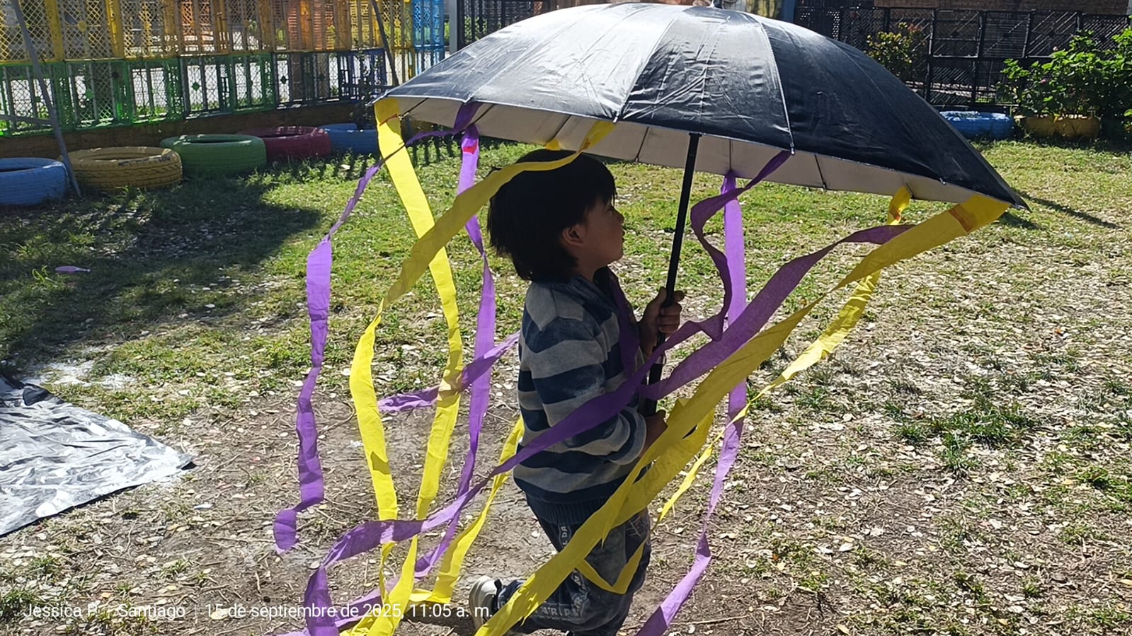 Niños jugando en jardín con paragua con tiras morada y amarilla
