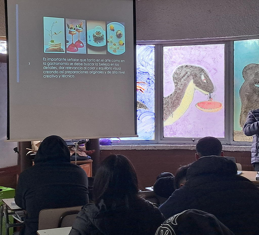 Jovenes viendo una presentación de un proyector. La presentación habla de la gastronomía y el arte