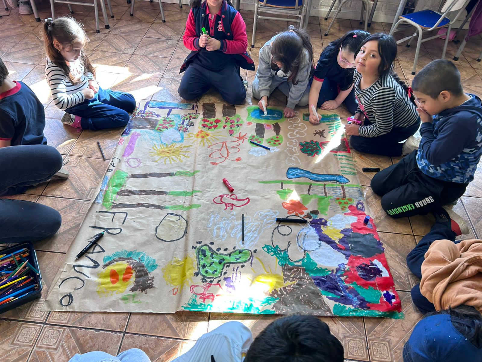 Niños sentados en el suelo dibujando en un papel craft grande