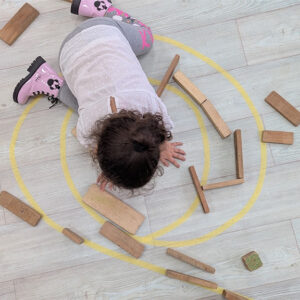 Niña dibujando en el suelo un espiral amarillo y está interactuando con bloques de madera