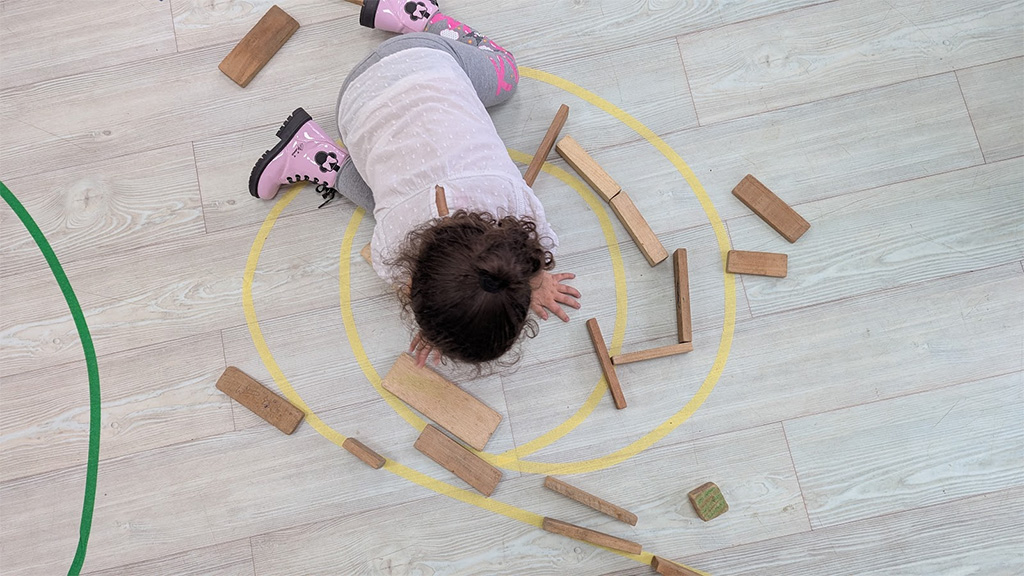 Niña dibujando en el suelo un espiral amarillo y está interactuando con bloques de madera