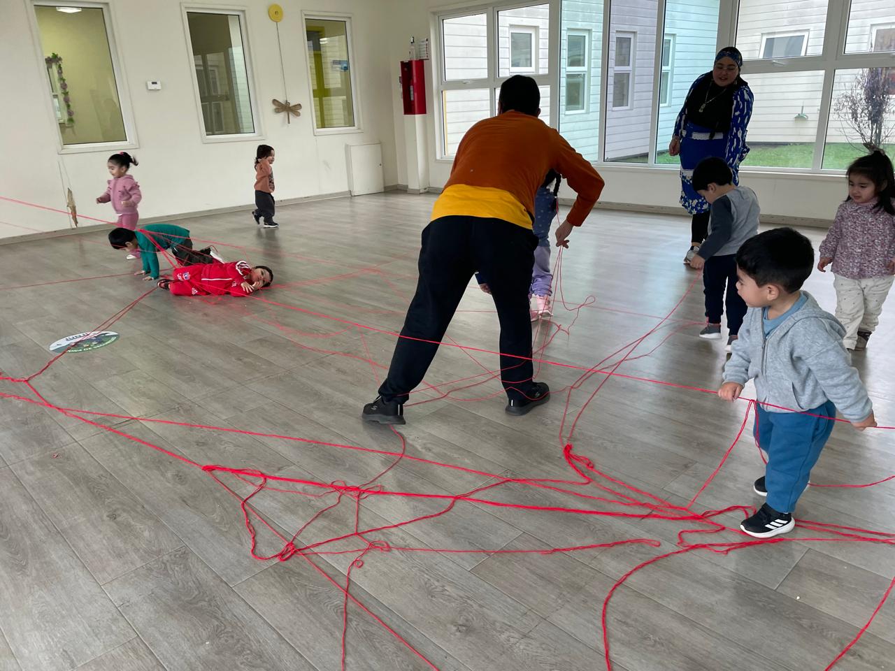 Niños haciendo una actividad con cordel rojo. Este se encuentra enredado y cada uno tiene una punta del cordel en sus manos.