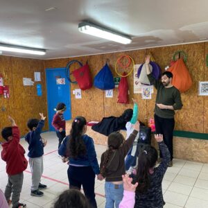 Niños de pie levantando la mano. Un profesor se encuentra frente a ellos también con la mano levantada