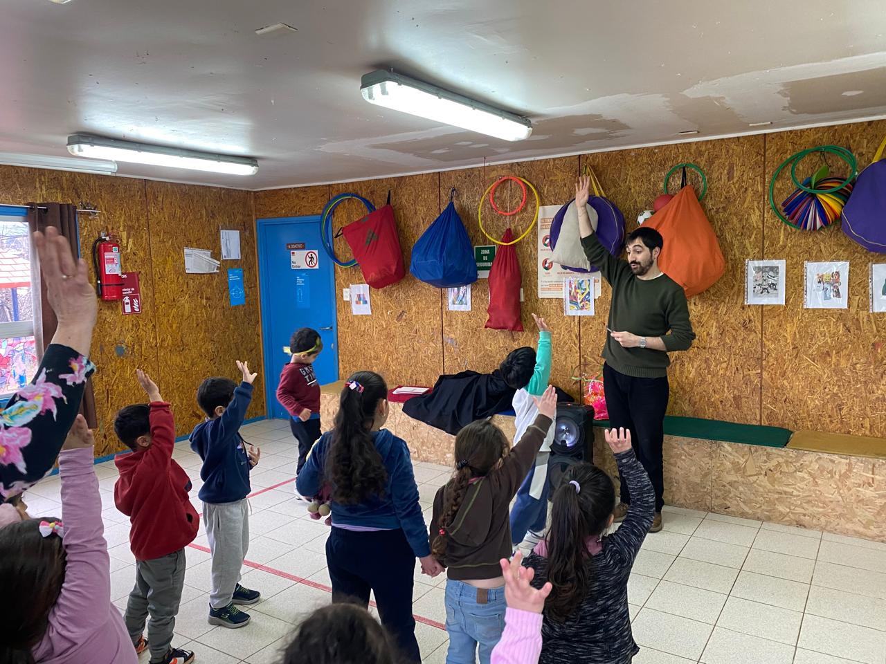 Niños de pie levantando la mano. Un profesor se encuentra frente a ellos también con la mano levantada