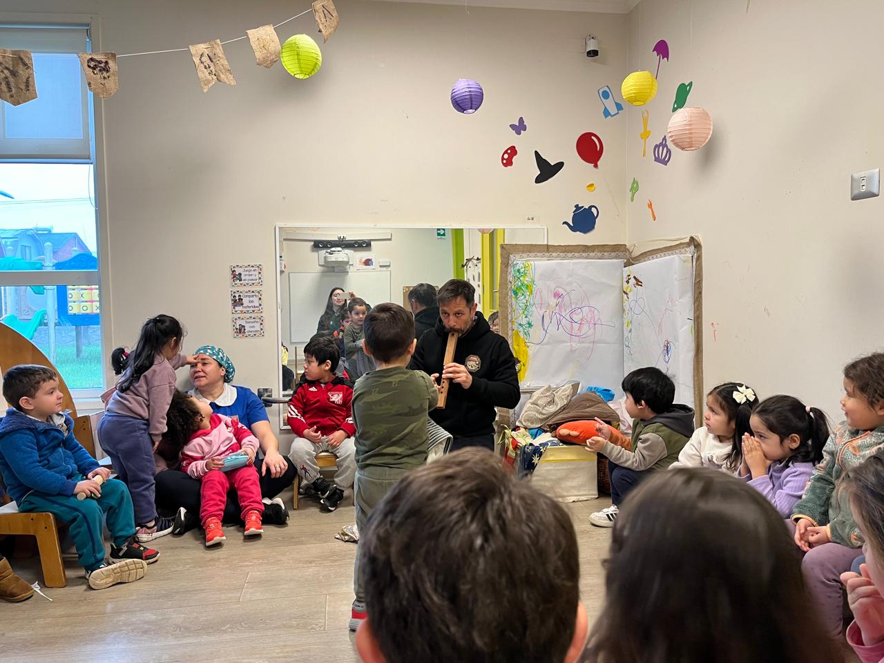 Niños sentados mientras un profesor toca una flauta de madera