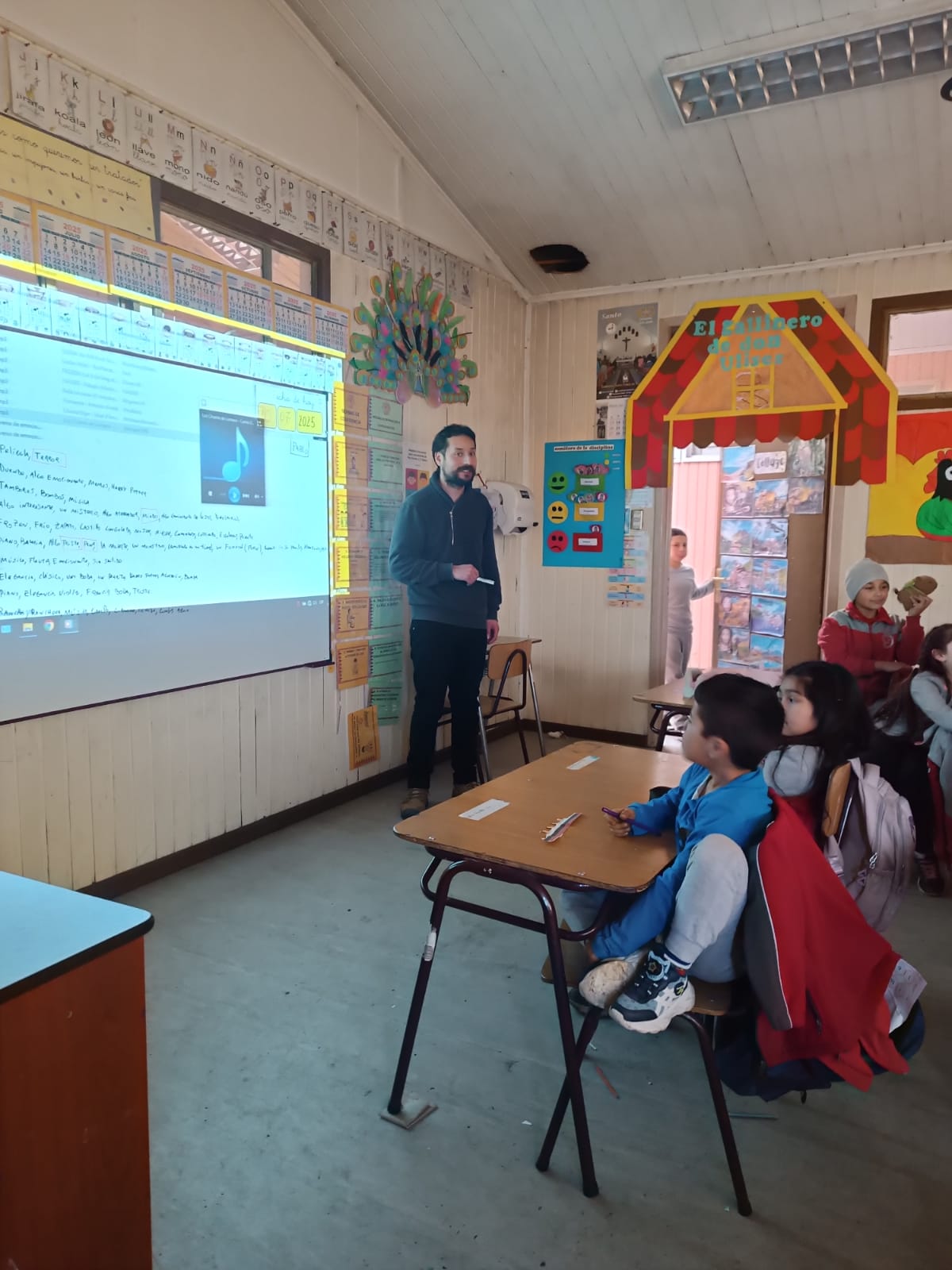 Profesor proyectando una presentación mientras niños lo observan sentados en su sillas