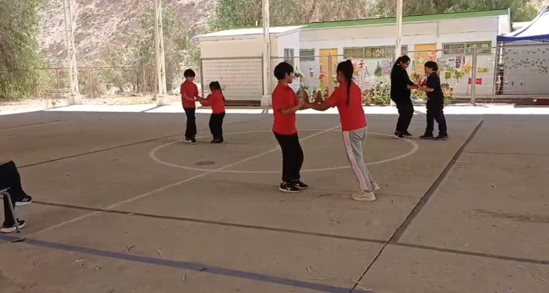 niños y niñas tomados de la mano bailando en una cancha