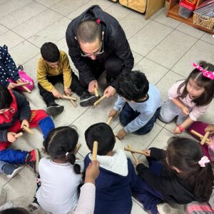 Niños pequeños jugando en el suelo con palitos, guiados por el profesor