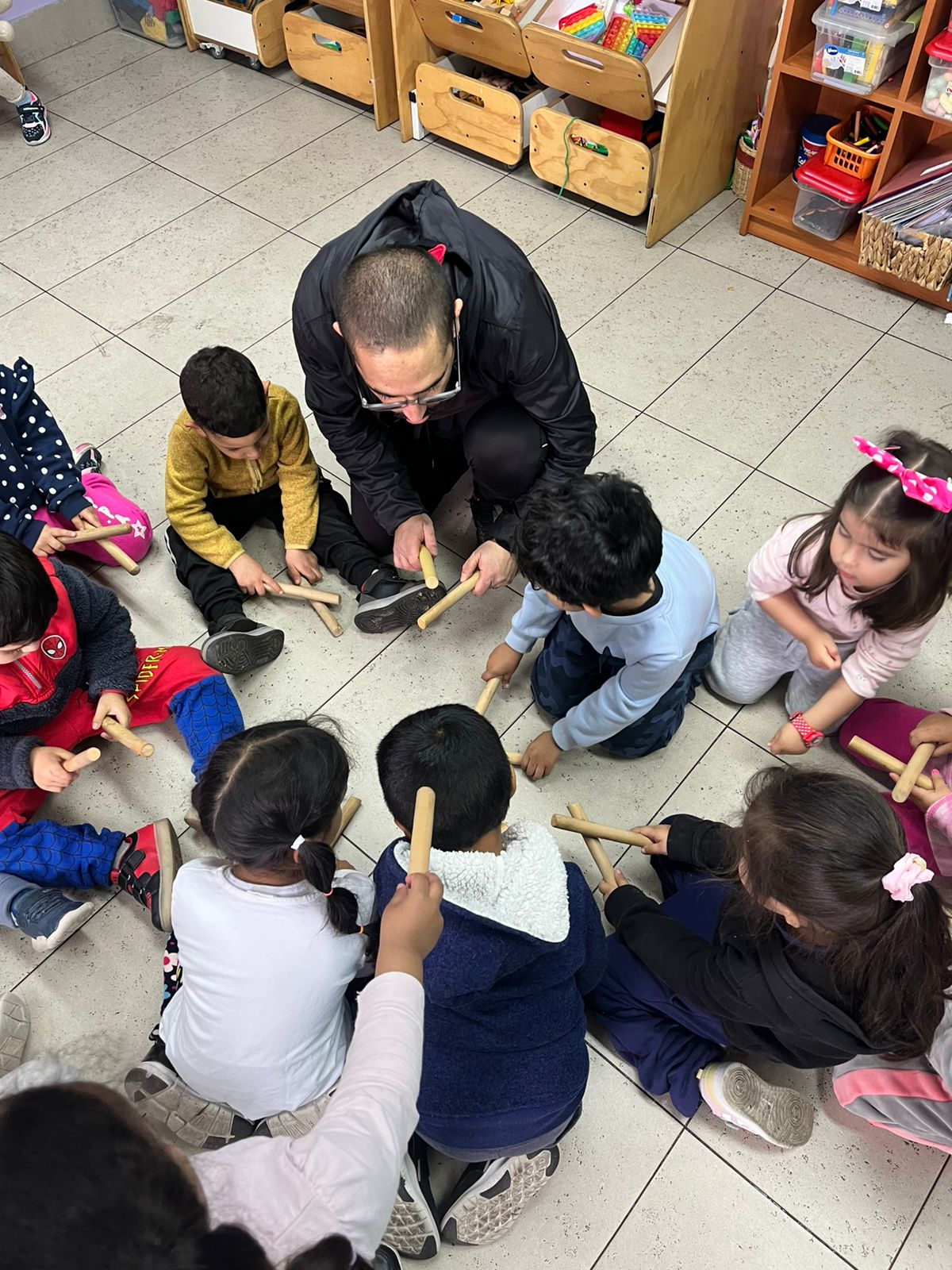 Niños pequeños jugando en el suelo con palitos, guiados por el profesor