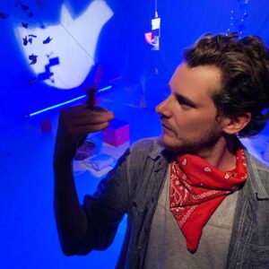 artista sosteniendo una pluma en un escenario con juegos de luces