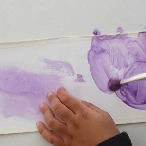 Manos de niño pintando con un pincel sobre un papel