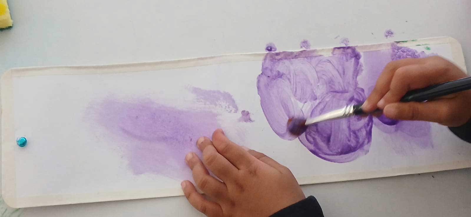 Manos de niño pintando con un pincel sobre un papel