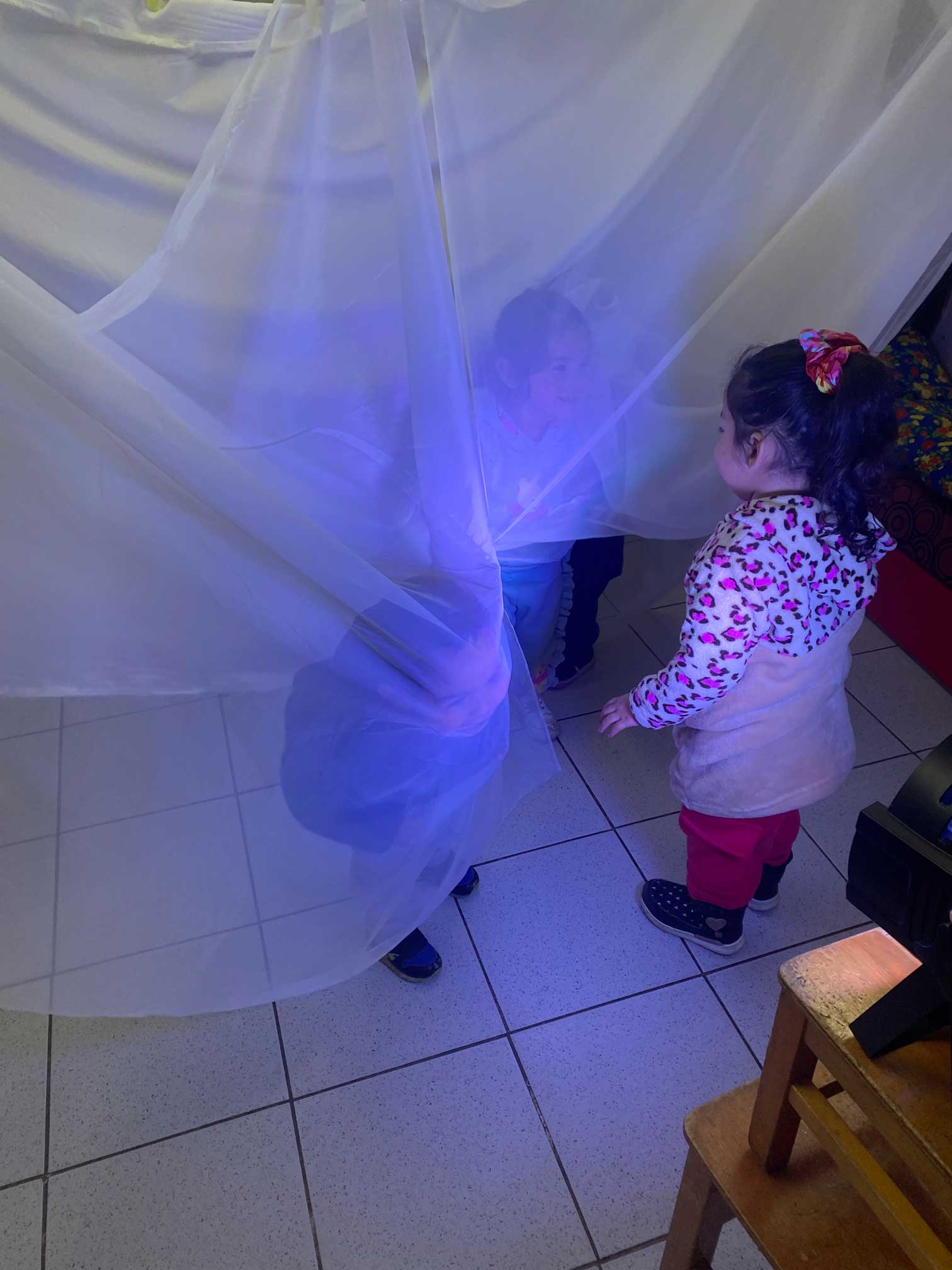 niños y niñas jugando con una tela transparente colgada