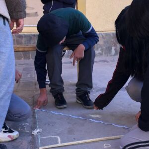 Jovenes trazando un triangulo en el suelo con una tiza