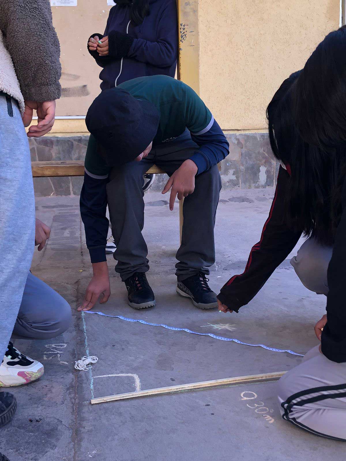 Jovenes trazando un triangulo en el suelo con una tiza