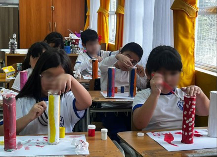 niños y niñas pintando con tempera unos tubos de carton
