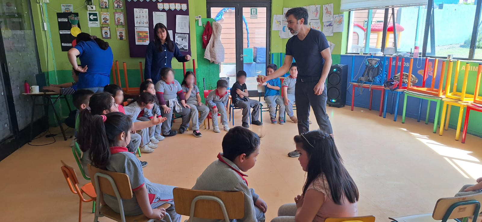 Niños sentados en sillas en medio circulo escuchando a un profesor