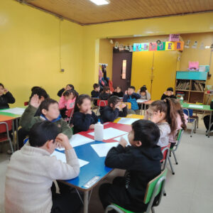 Niños sentados en mesas, se encuentran con hojas en blanco
