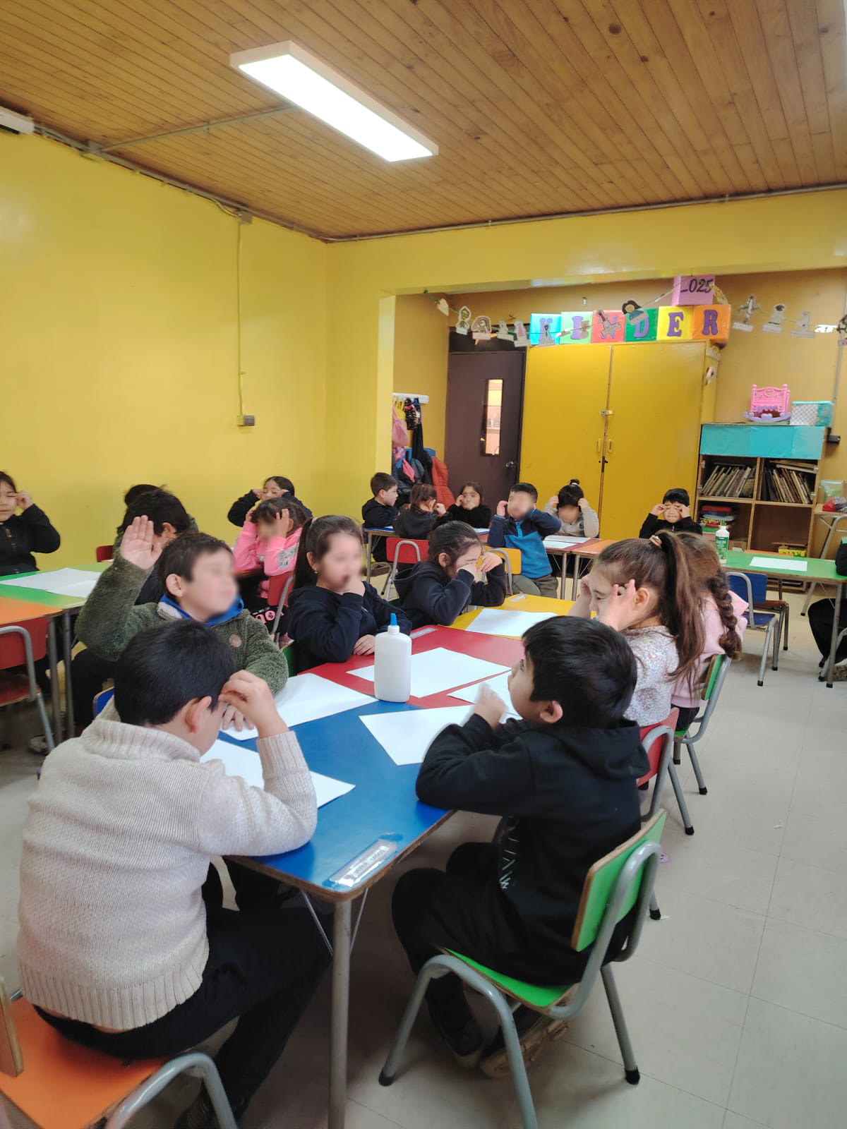 Niños sentados en mesas, se encuentran con hojas en blanco