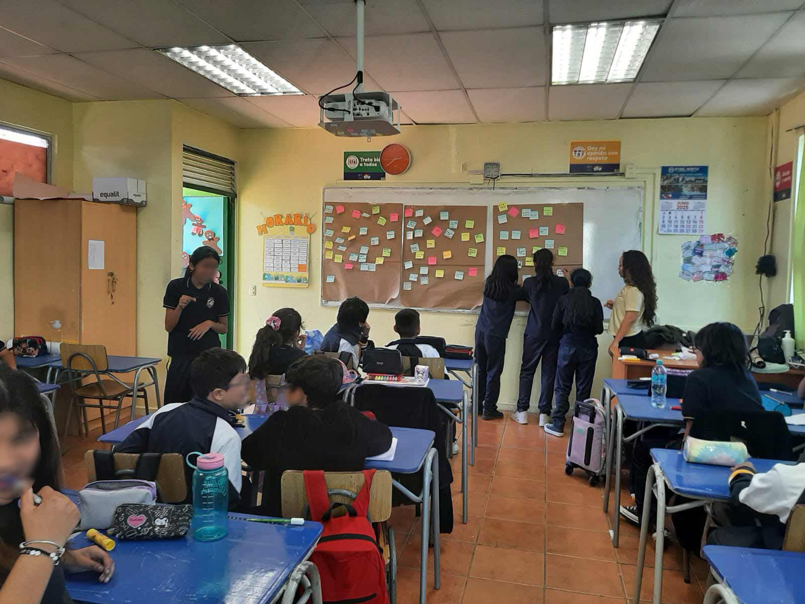 Tres niñas junto a su educadora poniendo unos papeles de colores en la pizarra